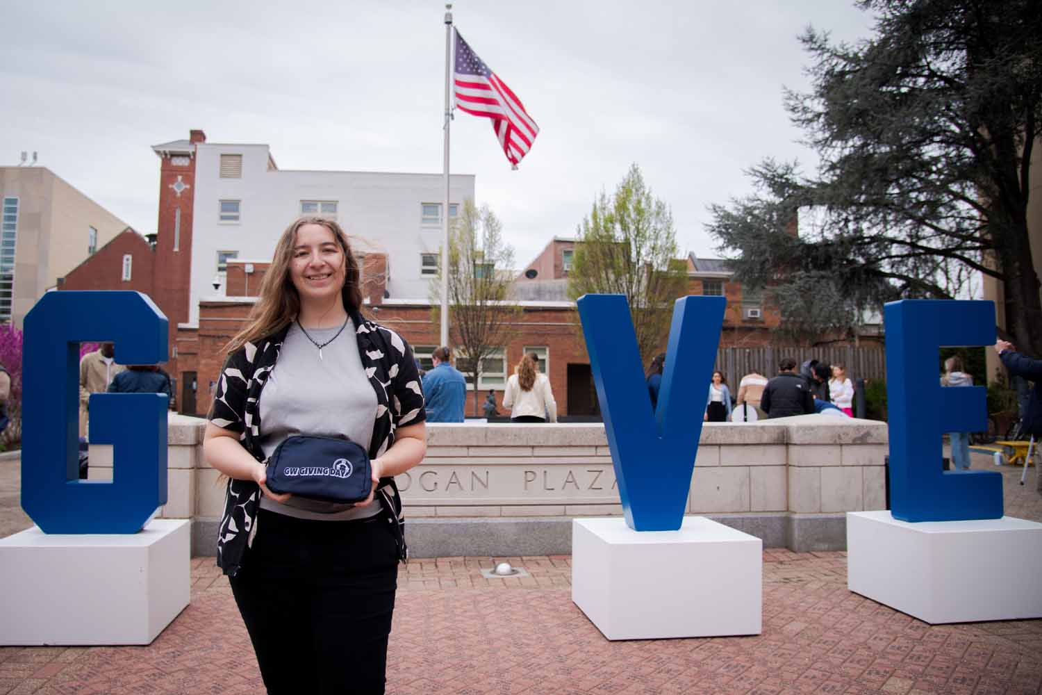 A person poses in Kogan Plaza in front of a "GIVE" statue on Giving Day 2025