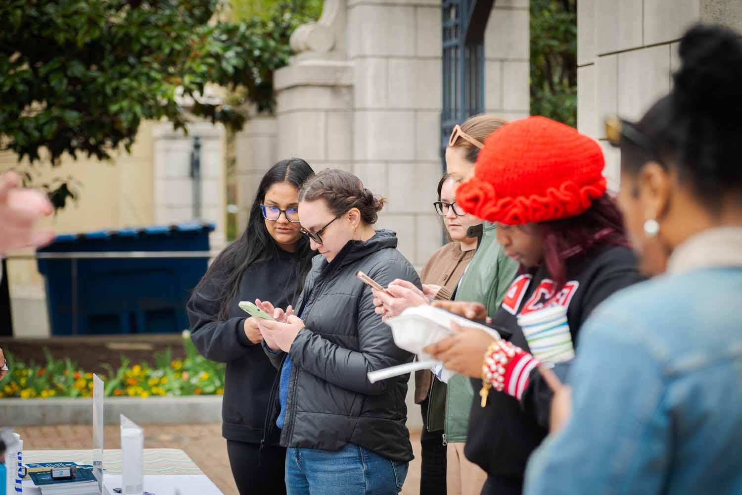 People on their phones on GW's campus on Giving Day 2025